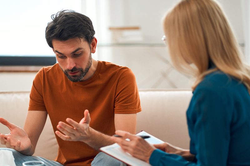 Young depressed man at the reception of a female psychologist during a mental health session. A man in frustrated feelings at a psychologist, being in a state of stress, talking about his problems.